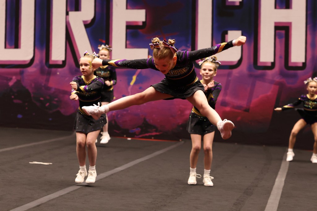 A junior cheerleader performing a toe touch